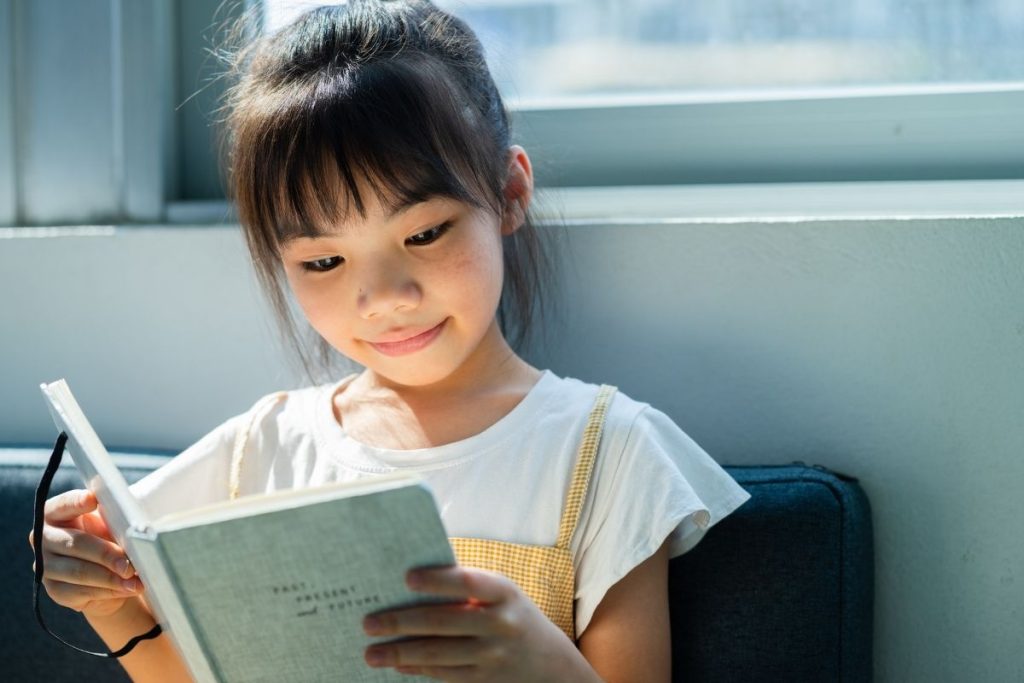Una niña leyendo un libro con cara feliz.