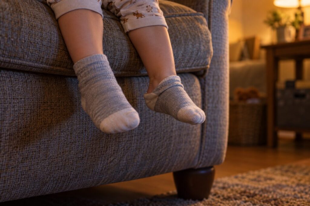 Los pies con calcetines de un niño pequeño asomando por el borde de un sillón grande