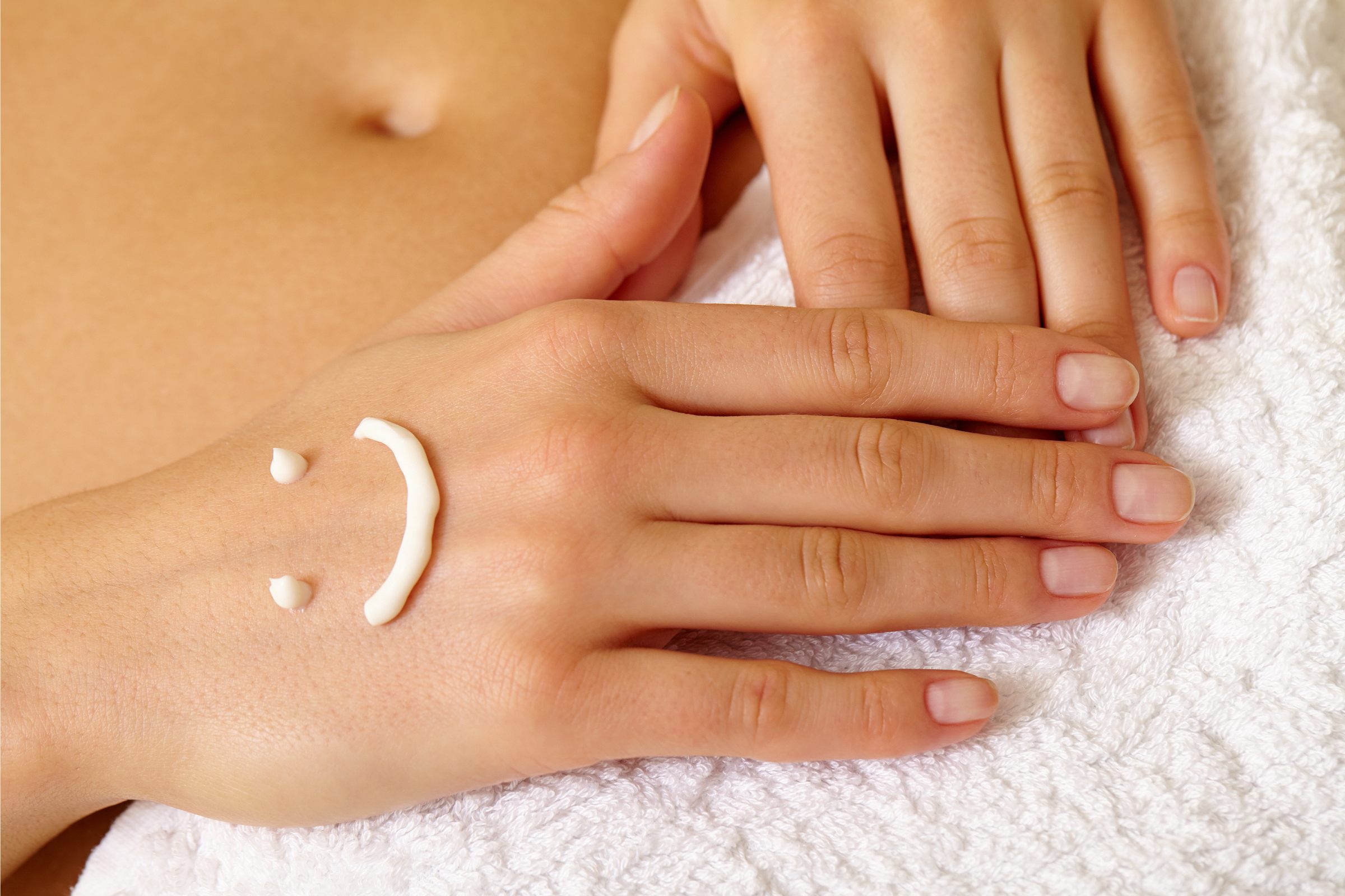 Manos cuidadas con uñas limpias descansando sobre una toalla blanca, con una carita sonriente dibujada con crema hidratante en el dorso de una de las manos.