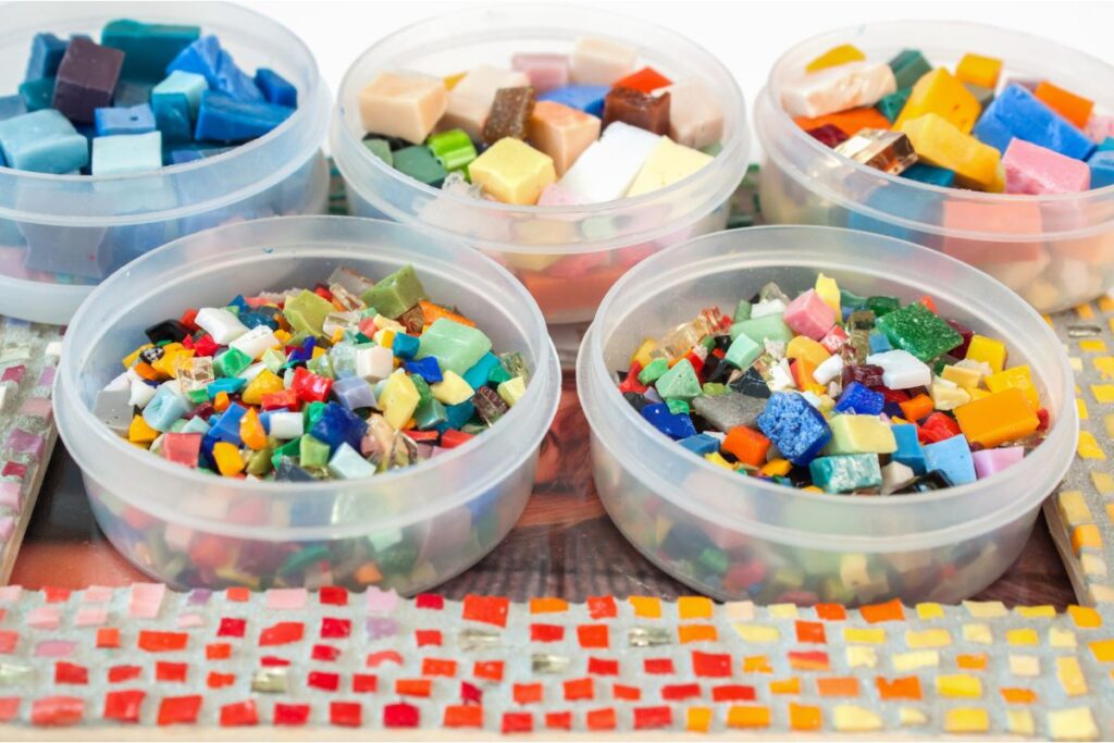 Recipientes con teselas de vidrio de distintos colores preparadas para crear mosaicos dentro de un marco para fotografías artesano.