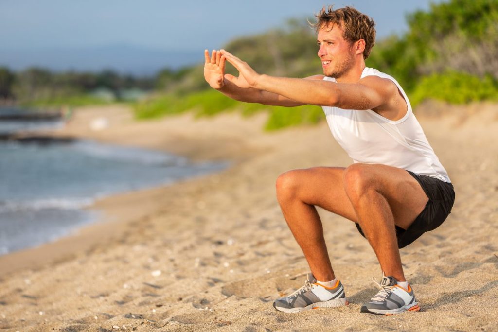 Un hombre joven haciendo sentadillas en la playa.