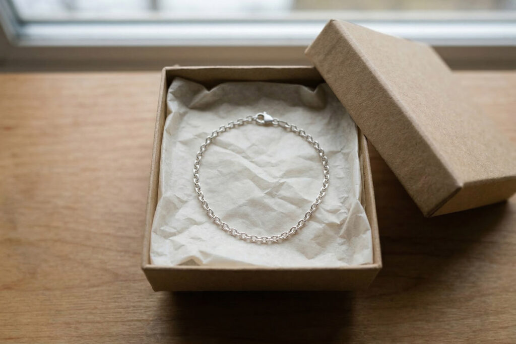 Una pulsera de plata en forma de cadena fina sobre papel de seda en una caja de cartón - imagen sintética.