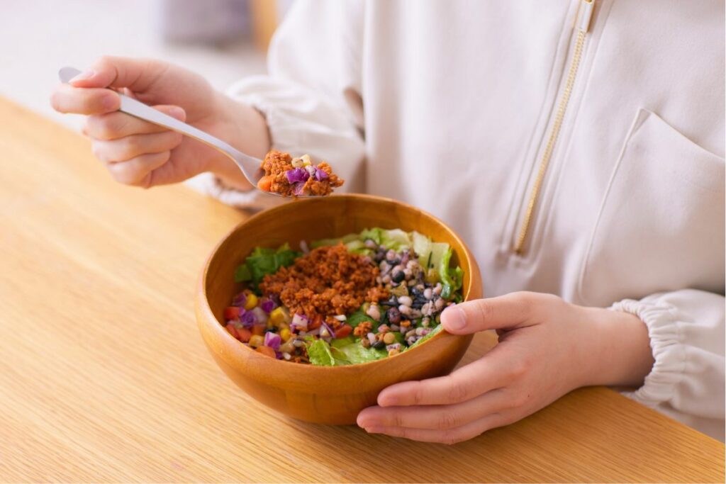 Una persona comiendo una ensalada con proteína vegetal como base.