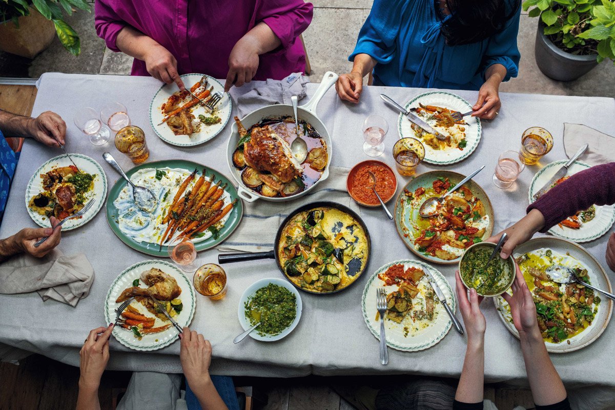 Vista superior de una mesa llena de platos y las manos de las personas comiendo.