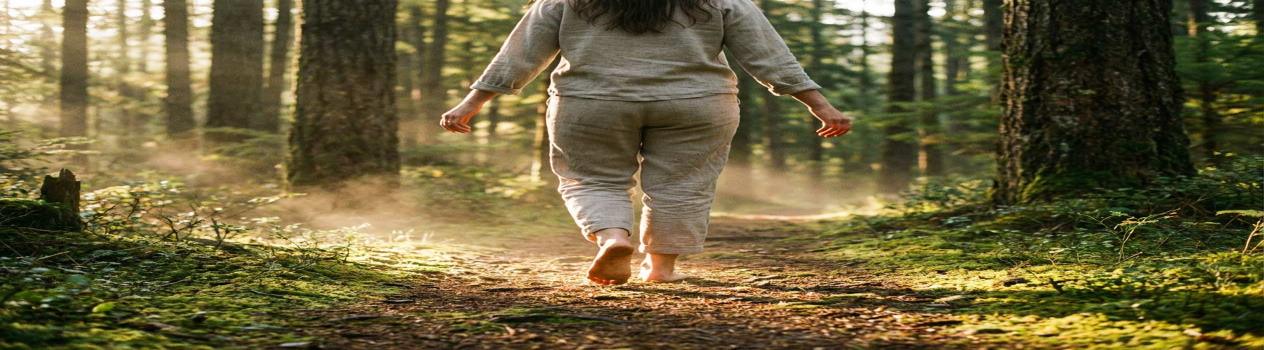 Una persona camina descalza por un sendero rodeado de árboles al amanecer, simbolizando la conexión con la naturaleza y la importancia del ejercicio para la salud mental y el bienestar.