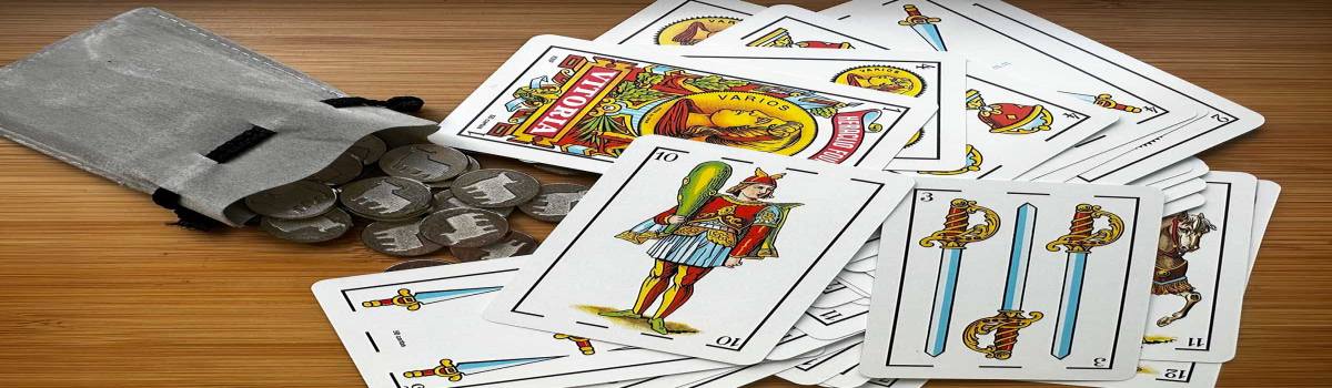 Cartas de una baraja española y amarracos para jugar al mus sobre una mesa de madera.