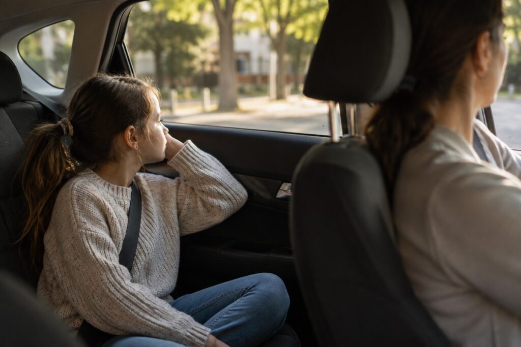 Niña sentada en la parte trasera de un coche mirando tranquilamente por la ventanilla.
